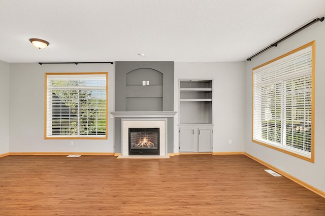 unfurnished living room featuring light wood-style floors, baseboards, built in shelves, and healthy amount of natural light