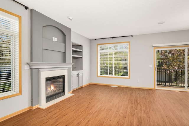 unfurnished living room featuring wood finished floors, baseboards, a glass covered fireplace, and built in features