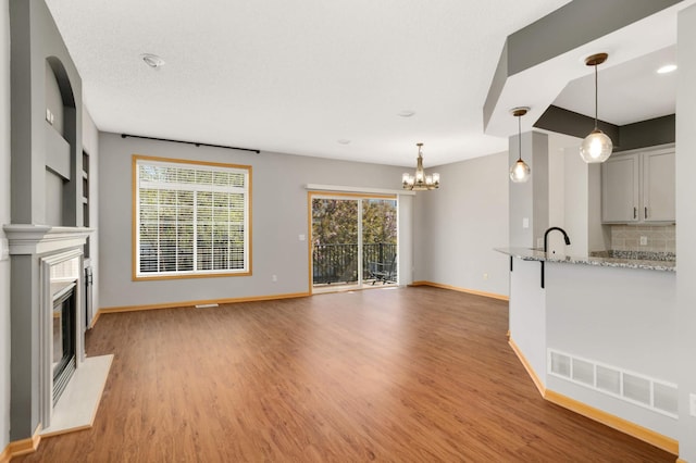 unfurnished living room with light wood-style floors, a chandelier, baseboards, and a glass covered fireplace