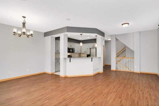 unfurnished living room featuring light wood-type flooring, baseboards, a chandelier, stairway, and recessed lighting