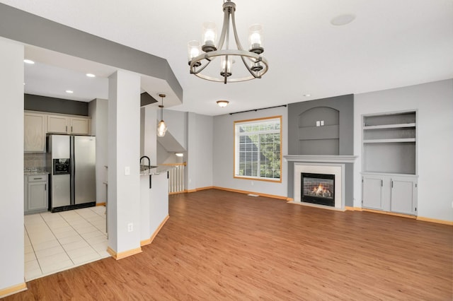 unfurnished living room with light wood-style floors, a chandelier, baseboards, built in shelves, and recessed lighting