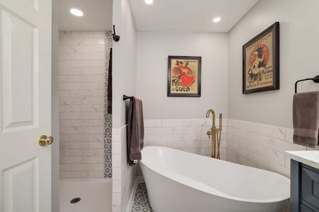 full bath featuring tile walls, a freestanding tub, tiled shower, recessed lighting, and vanity