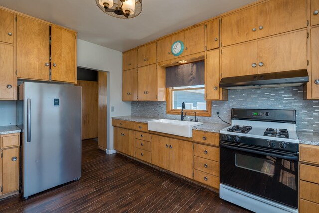kitchen featuring a sink, light countertops, freestanding refrigerator, under cabinet range hood, and gas range oven