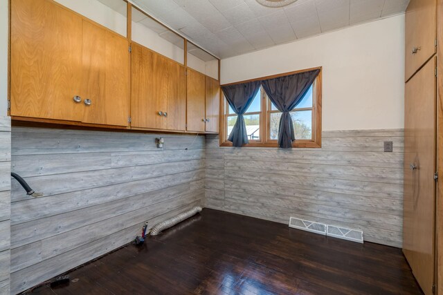 clothes washing area with wooden walls, dark wood-type flooring, and visible vents