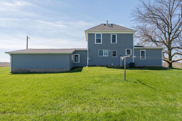 rear view of property with a yard, central AC unit, and a shingled roof