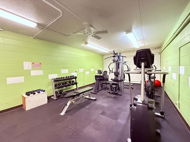 gym featuring a ceiling fan, a textured ceiling, and concrete block wall