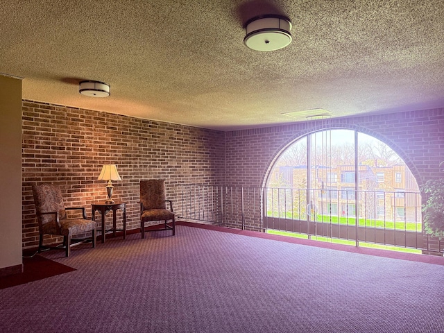 sitting room featuring carpet floors, a textured ceiling, brick wall, and baseboards