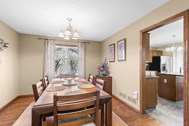 dining room featuring an inviting chandelier, a textured ceiling, baseboards, light wood-type flooring, and visible vents