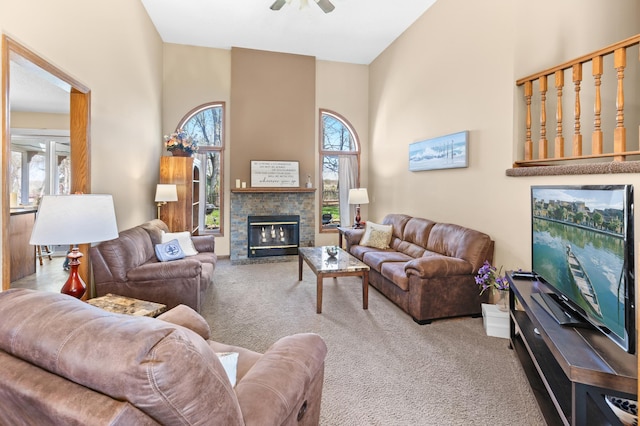 carpeted living area featuring a ceiling fan, a stone fireplace, and a towering ceiling