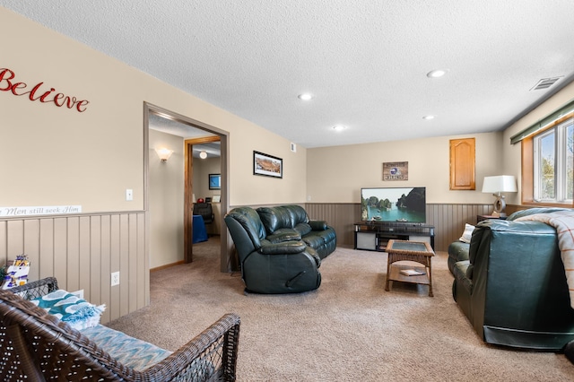living area with light colored carpet, a textured ceiling, visible vents, and wainscoting