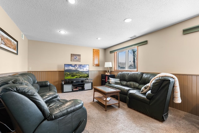 carpeted living room with wooden walls, a textured ceiling, visible vents, and a wainscoted wall