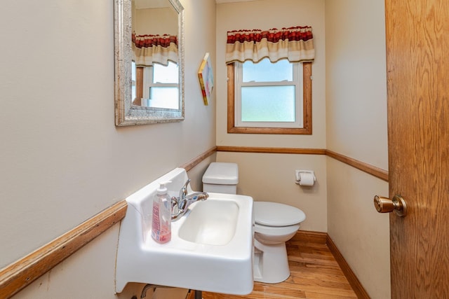 half bathroom with toilet, wood finished floors, baseboards, and a sink