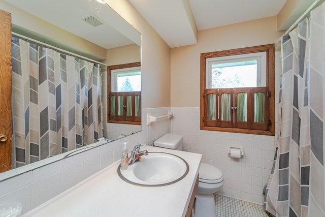 bathroom with tile walls, toilet, visible vents, tile patterned flooring, and wainscoting