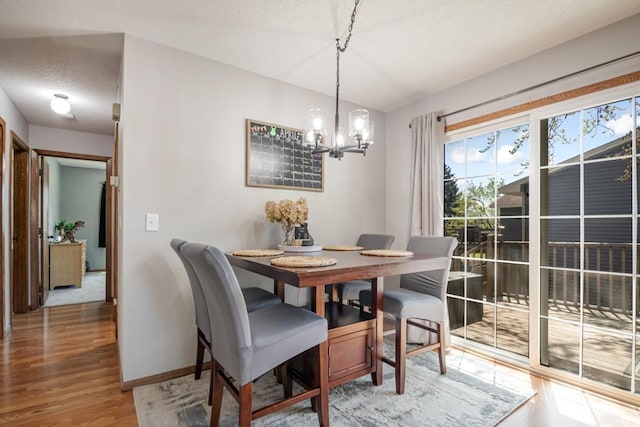dining room featuring baseboards, a textured ceiling, a chandelier, and light wood-type flooring