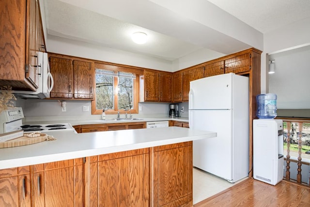 kitchen with a peninsula, white appliances, light countertops, brown cabinets, and a sink