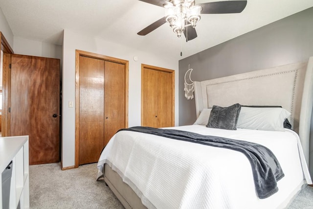 bedroom featuring light colored carpet, multiple closets, and ceiling fan