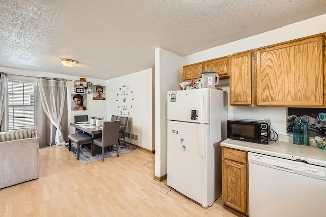 kitchen with light countertops, light wood-style flooring, white appliances, and a textured ceiling