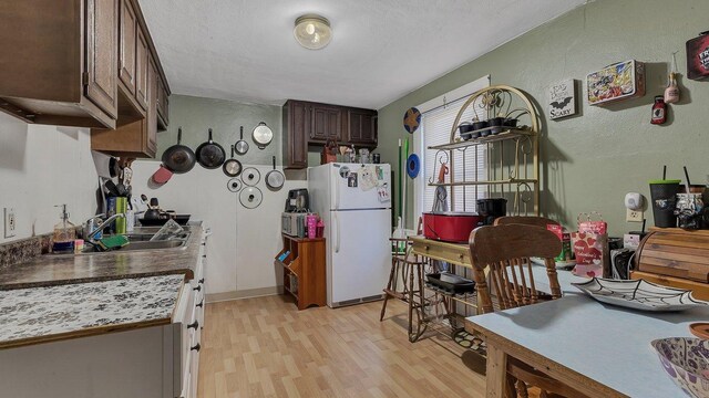 kitchen with freestanding refrigerator, a textured wall, dark brown cabinetry, a sink, and light wood finished floors