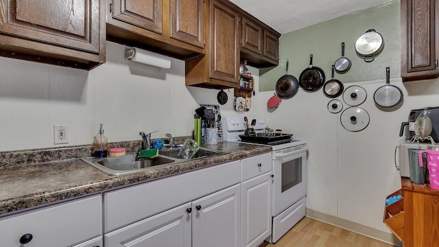 kitchen featuring dark countertops, light wood-style floors, white electric range, white cabinets, and a sink