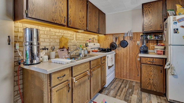 kitchen featuring a sink, white appliances, light countertops, brown cabinetry, and wood finished floors