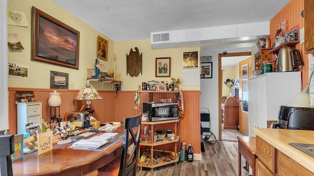 office area featuring wainscoting, a sink, wood walls, wood finished floors, and visible vents