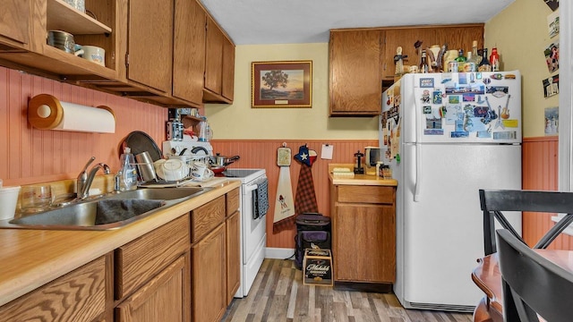 kitchen with a sink, white appliances, light countertops, brown cabinetry, and a wainscoted wall