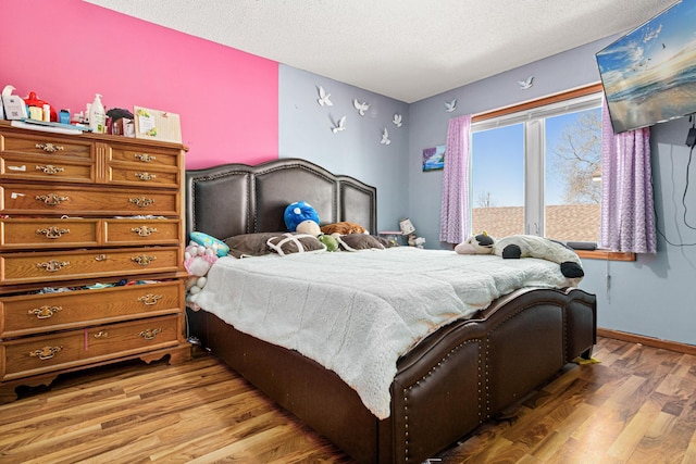 bedroom featuring baseboards, a textured ceiling, and wood finished floors