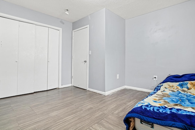 bedroom featuring a textured ceiling, baseboards, light wood-style flooring, and a closet