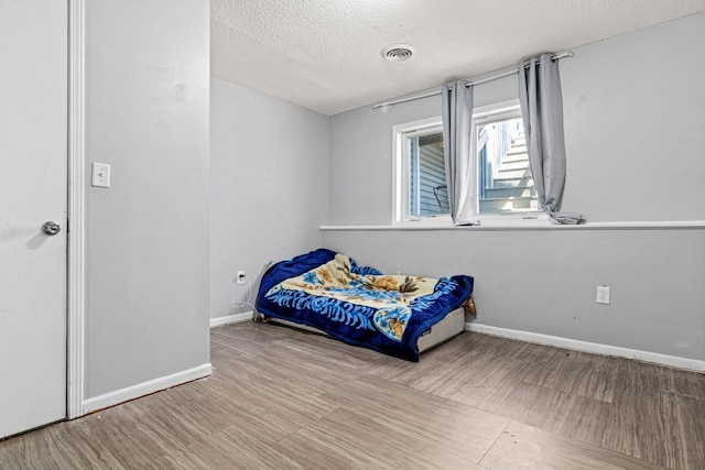 bedroom with a textured ceiling, visible vents, baseboards, and wood finished floors