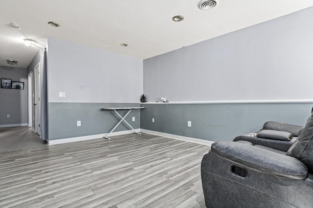 living area featuring baseboards, a textured ceiling, visible vents, and wood finished floors