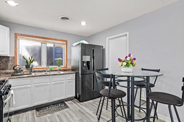 kitchen featuring a sink, light wood finished floors, stainless steel appliances, white cabinetry, and visible vents