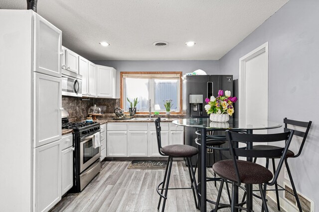 kitchen featuring stainless steel appliances, white cabinetry, a sink, and light wood-type flooring