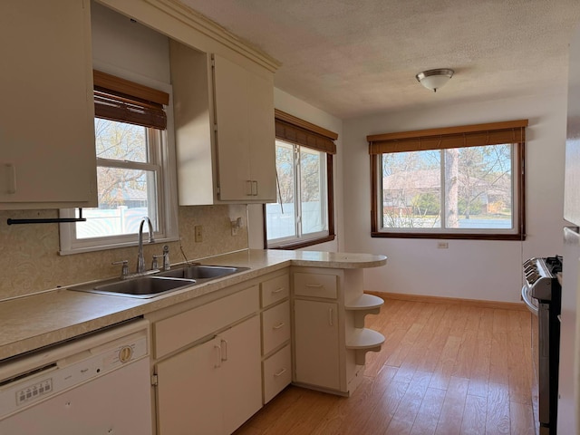kitchen featuring open shelves, stainless steel gas stove, white dishwasher, light countertops, and a sink