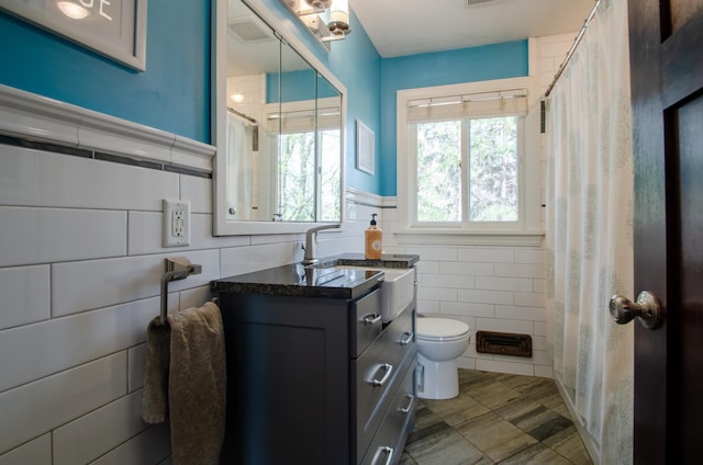 bathroom with tile walls, curtained shower, a wainscoted wall, vanity, and toilet