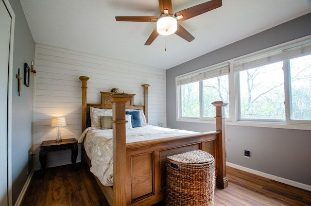 bedroom with baseboards, ceiling fan, wood walls, and dark wood-style floors
