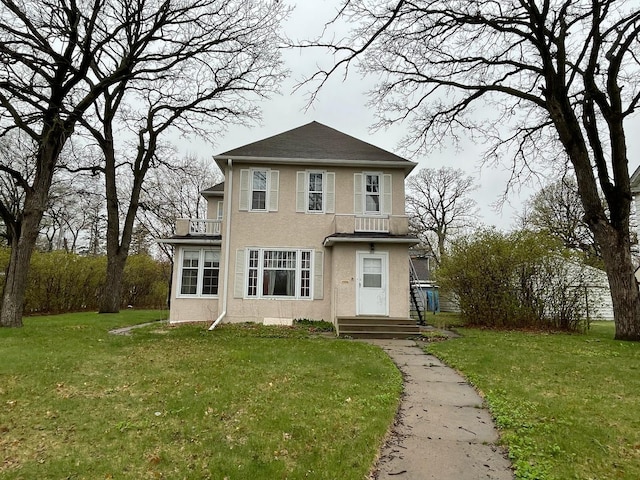 traditional home with a balcony, stucco siding, and a front yard