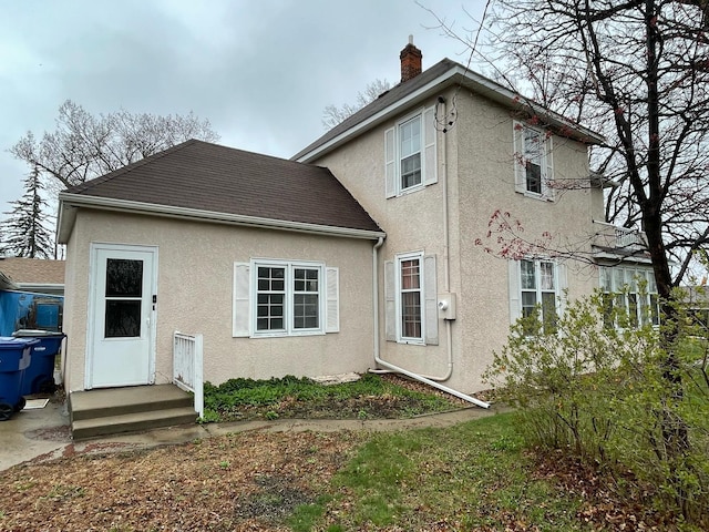 rear view of property featuring stucco siding and a chimney
