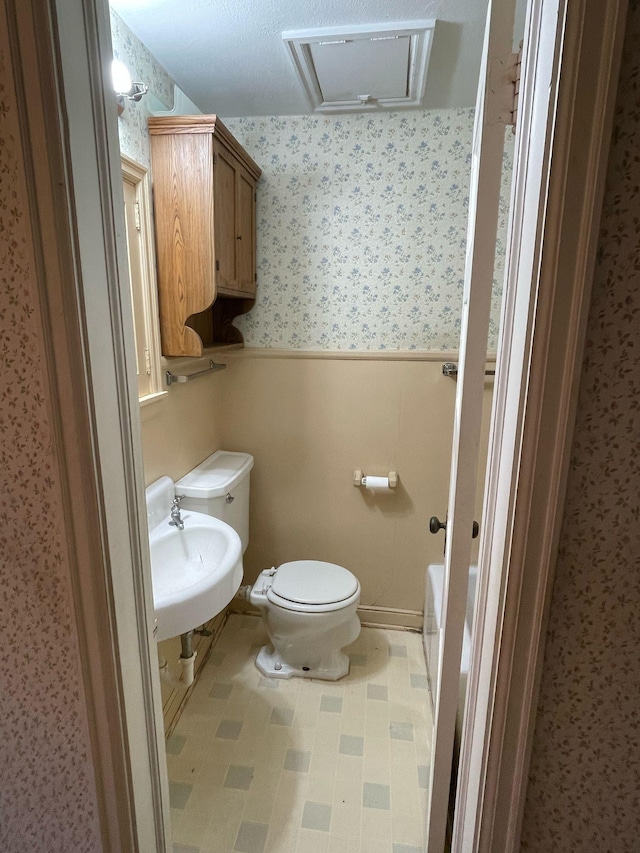 bathroom featuring a washtub, a sink, a wainscoted wall, toilet, and wallpapered walls