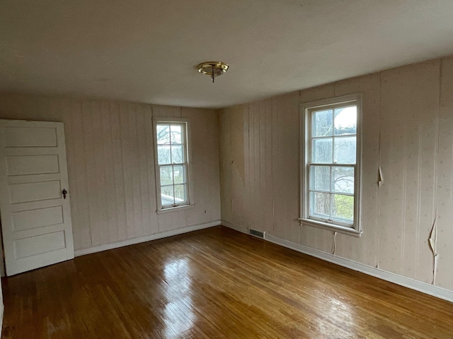 spare room featuring baseboards, wood walls, wood finished floors, and visible vents