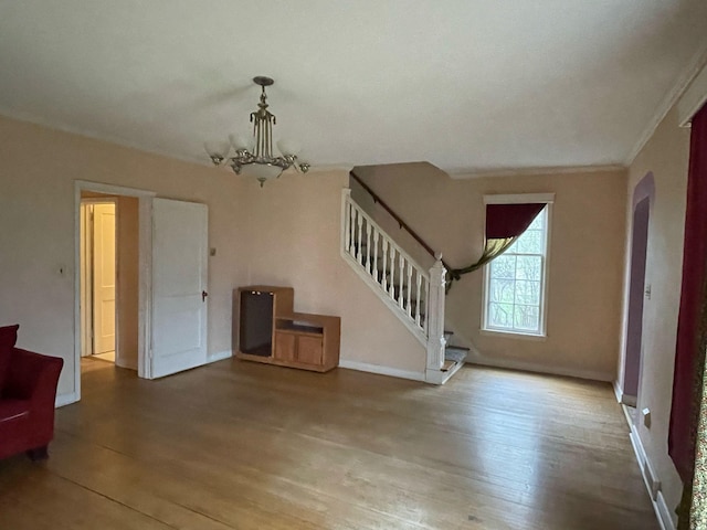 unfurnished living room with wood finished floors, stairway, baseboards, a notable chandelier, and ornamental molding