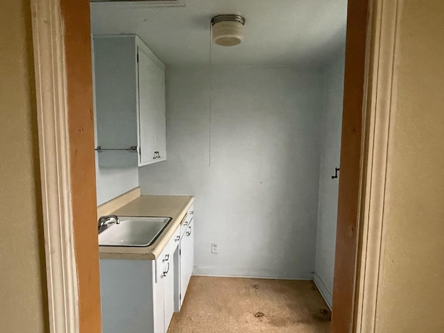 kitchen featuring light countertops, white cabinets, light carpet, and a sink