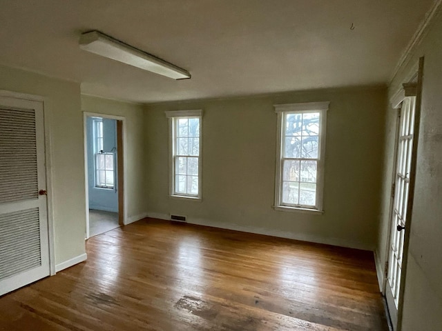 unfurnished room featuring baseboards, visible vents, plenty of natural light, and wood finished floors