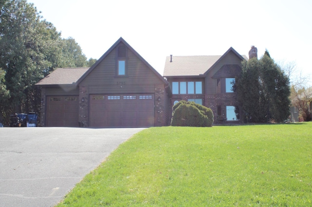 view of front facade with a chimney, driveway, brick siding, an attached garage, and a front yard