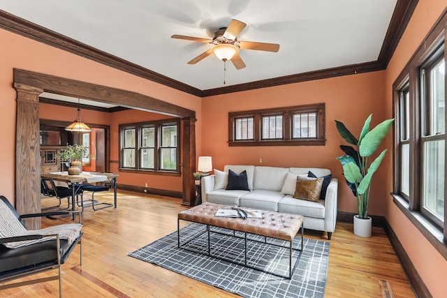 living area featuring baseboards, ornamental molding, light wood finished floors, and a ceiling fan