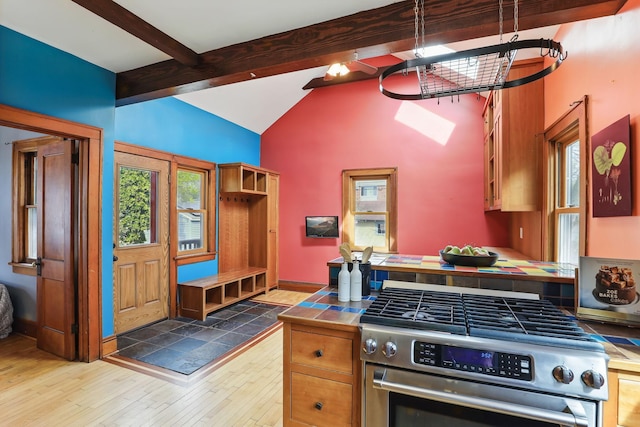 kitchen with beam ceiling, glass insert cabinets, stainless steel gas range oven, tile countertops, and hardwood / wood-style flooring
