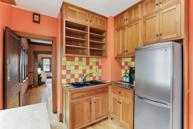 kitchen featuring freestanding refrigerator, decorative backsplash, a sink, and light wood-type flooring