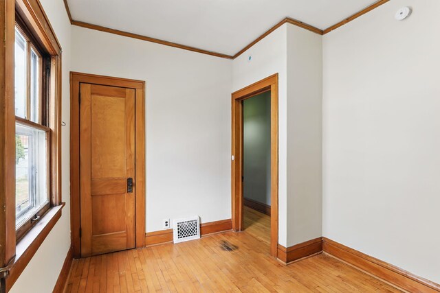 spare room featuring crown molding, baseboards, light wood finished floors, and visible vents