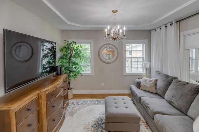 living room featuring light wood-style floors, a raised ceiling, baseboards, and a chandelier