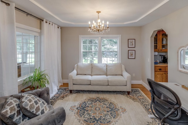 living area featuring a raised ceiling, plenty of natural light, wood finished floors, and a notable chandelier