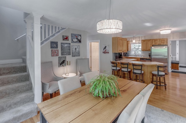 dining space featuring light wood-style flooring, stairs, and a notable chandelier